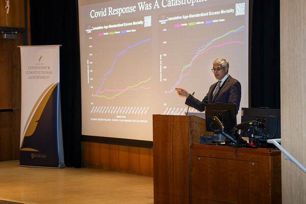 Dr. Jay Bhattacharya gestures toward a projected graph. A banner for the Center for Citizenship & Constitutional Government stands to the left.