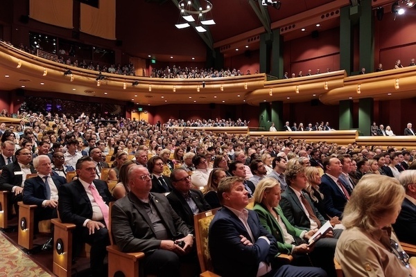 A large audience sits in the wooden seats of the DeBartolo Performing Arts Center at the University of Notre Dame.  Attendees are dressed in business attire and attentively watch a performance or presentation.