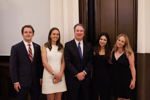 Justice Brett Kavanaugh, in a blue tie, smiles with a male student in a striped tie and three female students.